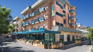 Un hotel de varios pisos con un diseño moderno, que cuenta con balcones en cada planta, una entrada cubierta y un cielo despejado.