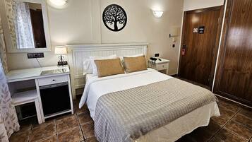 Una habitación de hotel con cama, mesita de noche, lámpara y un adorno de árbol en la pared.