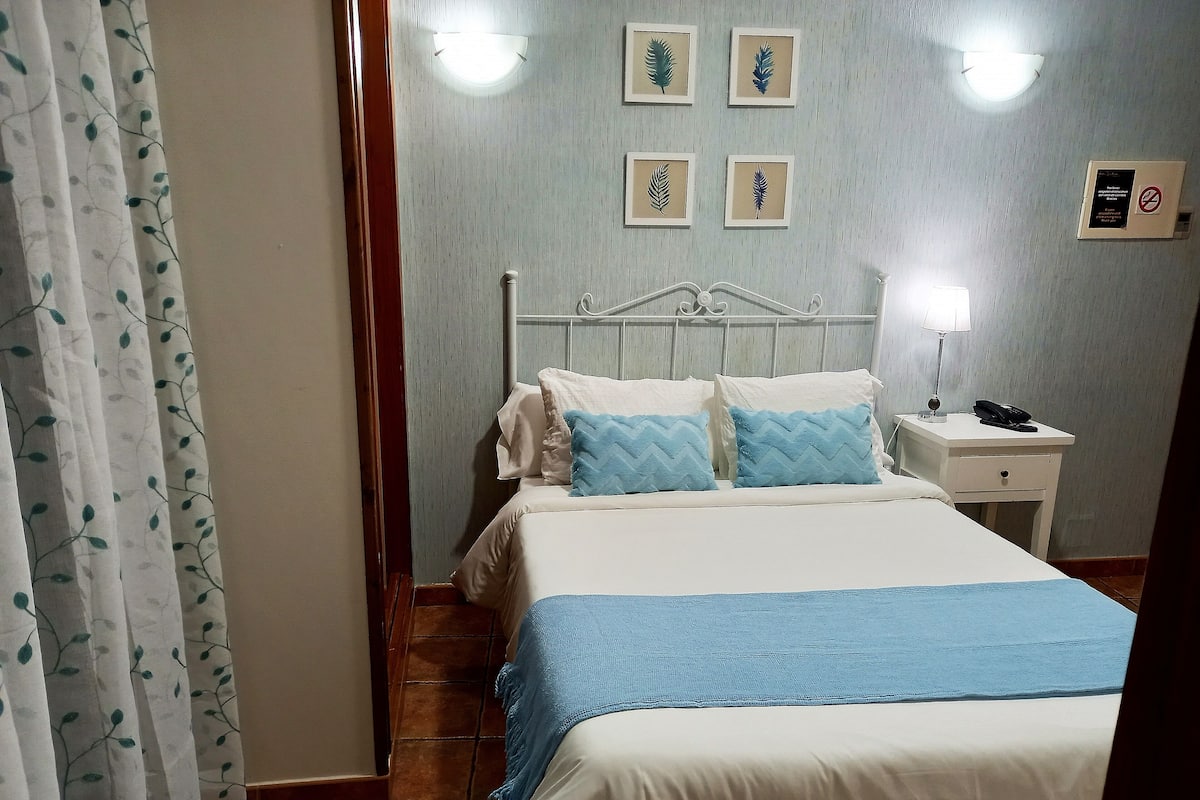 A hotel room with a bed, nightstand, and wall-mounted light fixture.