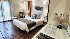 Una habitación de hotel con una cama grande, una mesita de noche, una lámpara, una obra de arte en la pared y un jarrón con plantas secas.
