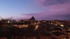 Un paisaje urbano al atardecer con edificios iluminados y una estructura abovedada destacada.
