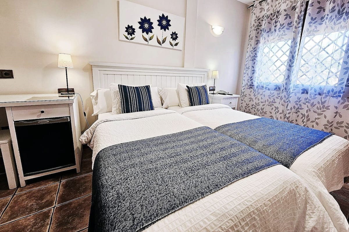A hotel room with a bed, bedside tables, a desk, and a window with curtains.