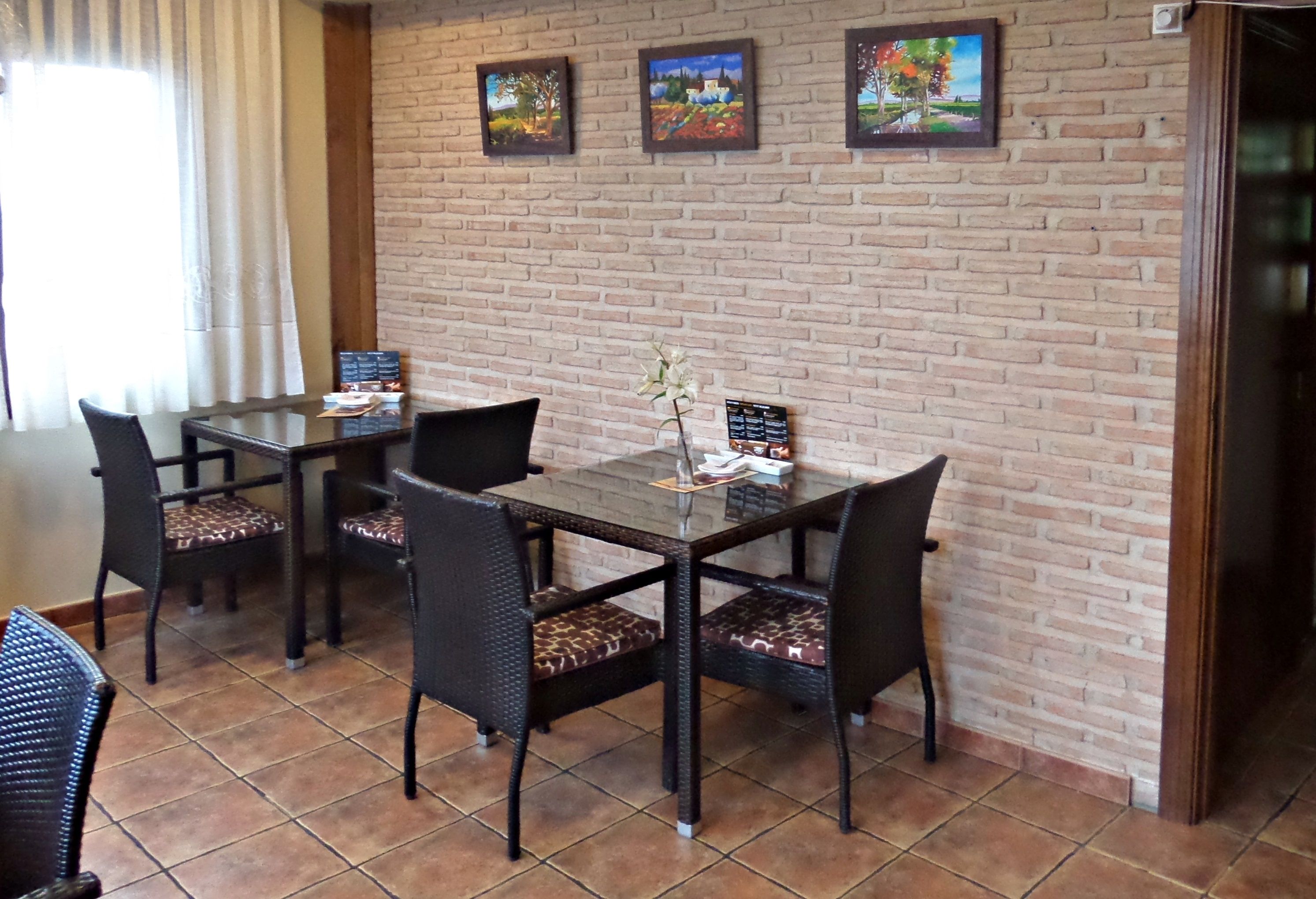 Un comedor con pared de ladrillo, tres cuadros enmarcados y una mesa con sillas.