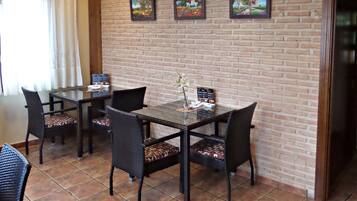 Un comedor con pared de ladrillo, tres cuadros enmarcados y una mesa con sillas.