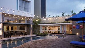 Un área de piscina moderna al aire libre con cubierta de madera, luces colgantes y asientos.