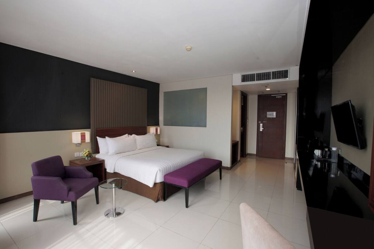 A modern hotel room with a large bed, a desk, a chair, and a TV.