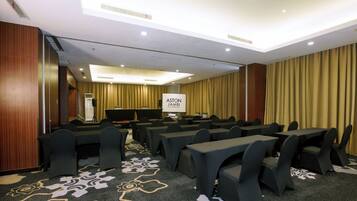 Un salón de conferencias con filas de mesas y sillas, una pantalla de proyector y una alfombra con estampado floral.
