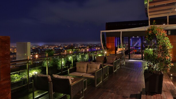 Una terraza en la azotea con mobiliario exterior, vistas a la ciudad y barandilla de cristal.