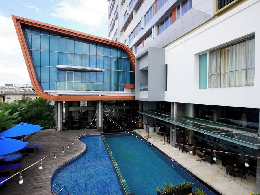 A modern hotel with a swimming pool, outdoor seating, and a unique curved glass facade.