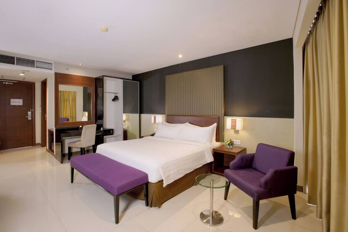 A hotel room with a bed, a desk, a chair, and a small table.
