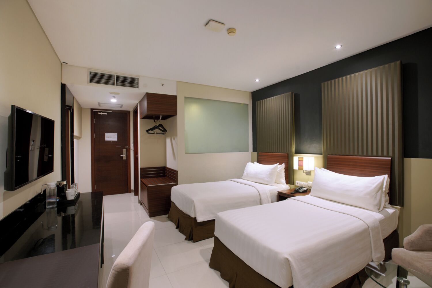 A hotel room with two beds, a TV, a minibar, and a seating area.