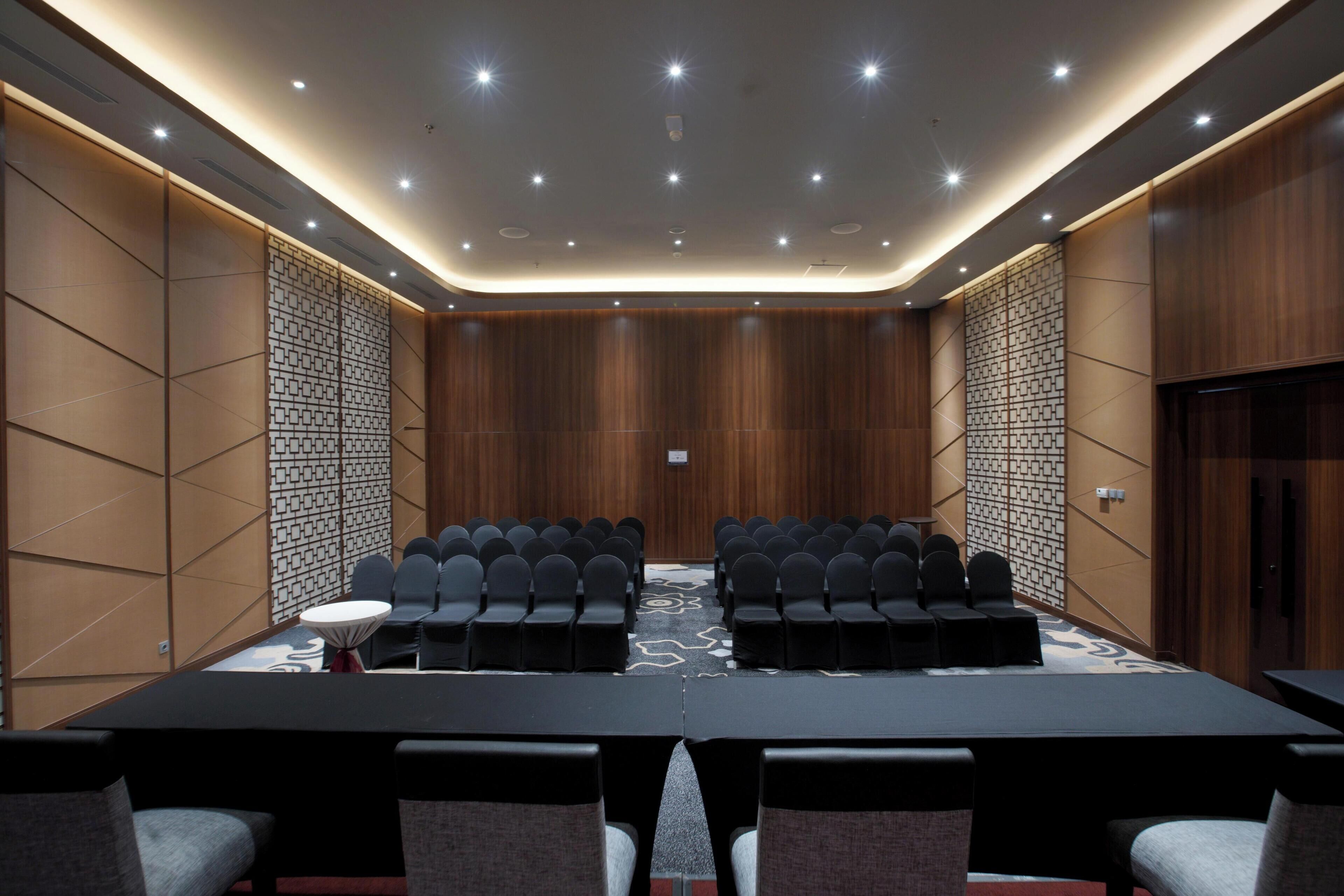 Une salle de conférence avec une longue table, des rangées de chaises et un mur orné de motifs.