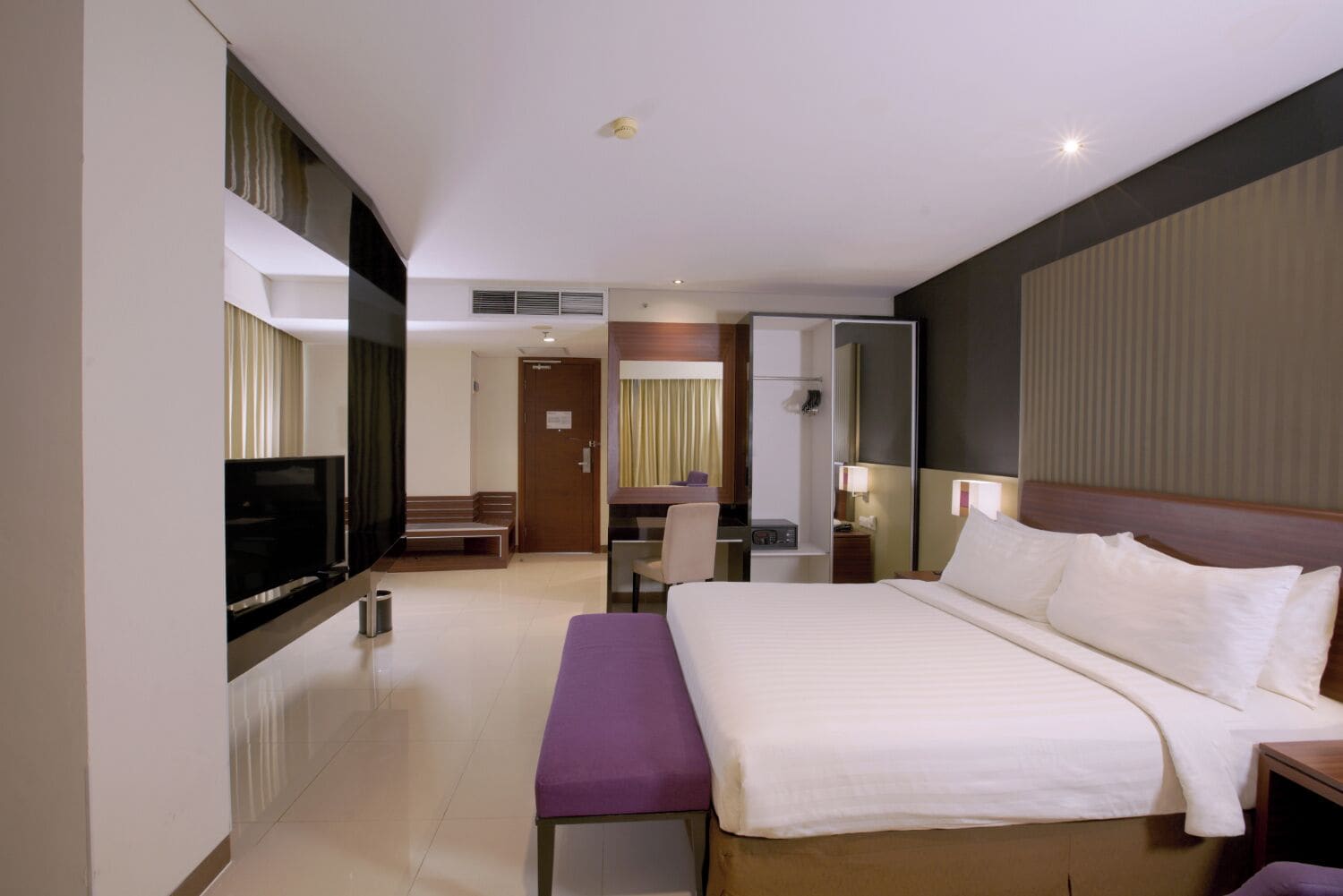 A hotel room with a large bed, a desk, a chair, a television, and a mirror.
