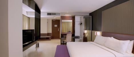 A hotel room with a large bed, a desk, a chair, a television, and a mirror.