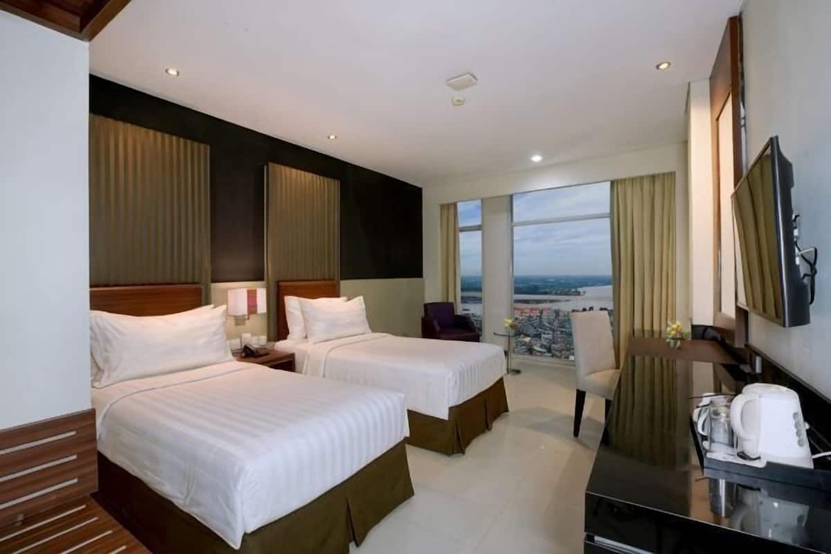 A hotel room with two beds, a desk, a chair, a TV, and a large window with a city view.