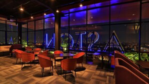 Un moderno salón con vista a la ciudad, con sillas y mesas rojas, y un gran letrero iluminado.
