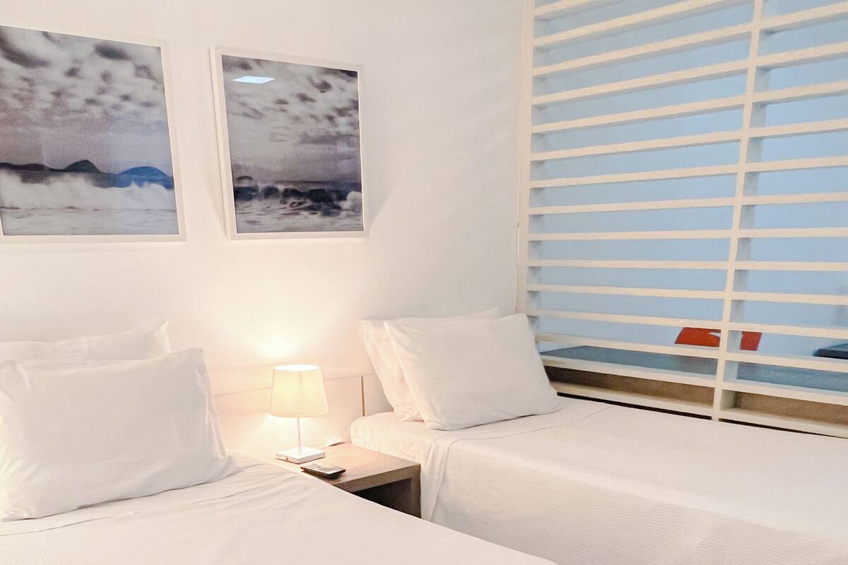 Una habitación de hotel con dos camas, una mesita de noche con lámpara y dos cuadros en la pared.