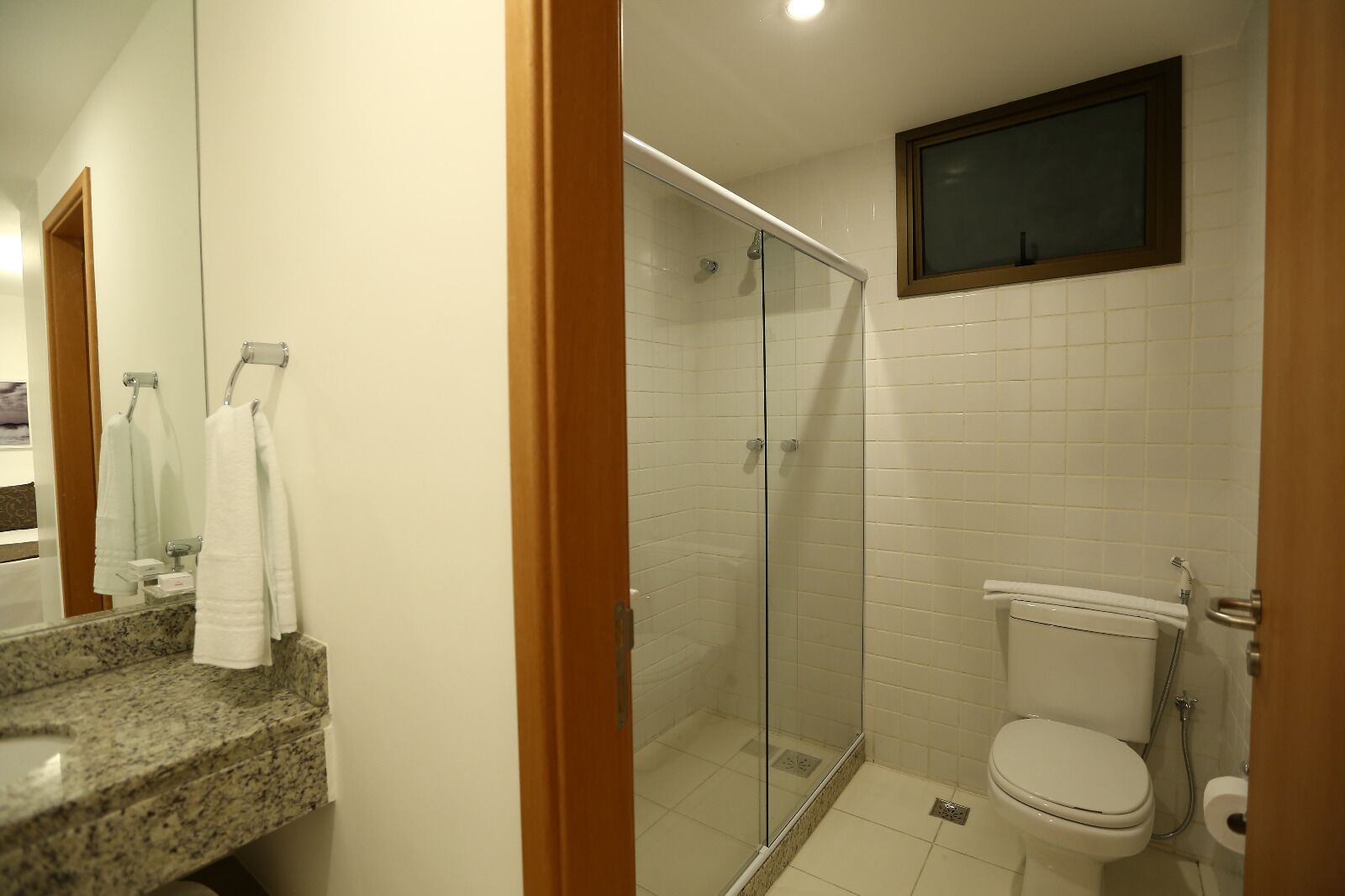 A bathroom with a glass shower enclosure, a toilet, and a marble countertop.