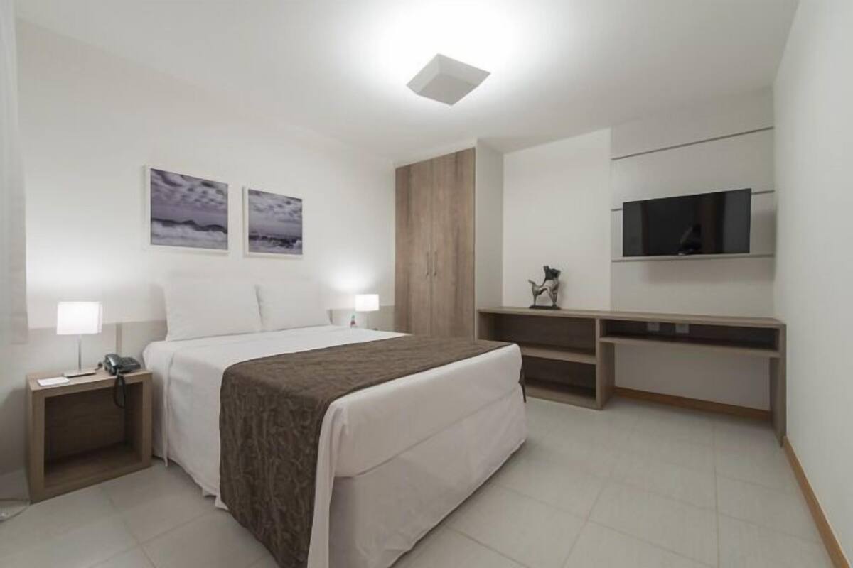 Una habitación de hotel moderna con una cama grande, mesitas de noche, un escritorio, un televisor y obras de arte en las paredes.