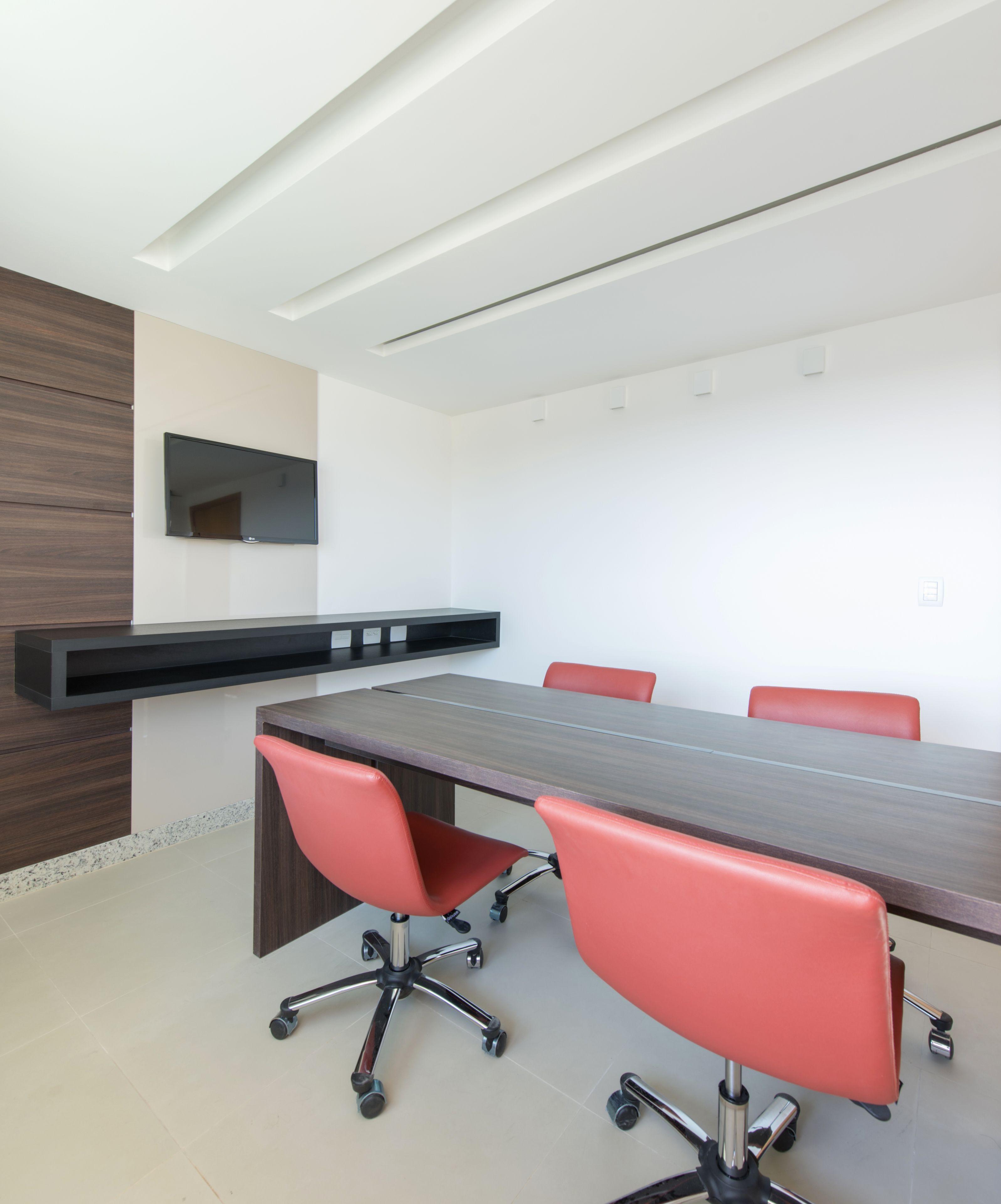 Una sala conferenze con un lungo tavolo, quattro sedie rosse, un televisore nero a parete e una parete decorativa in legno.