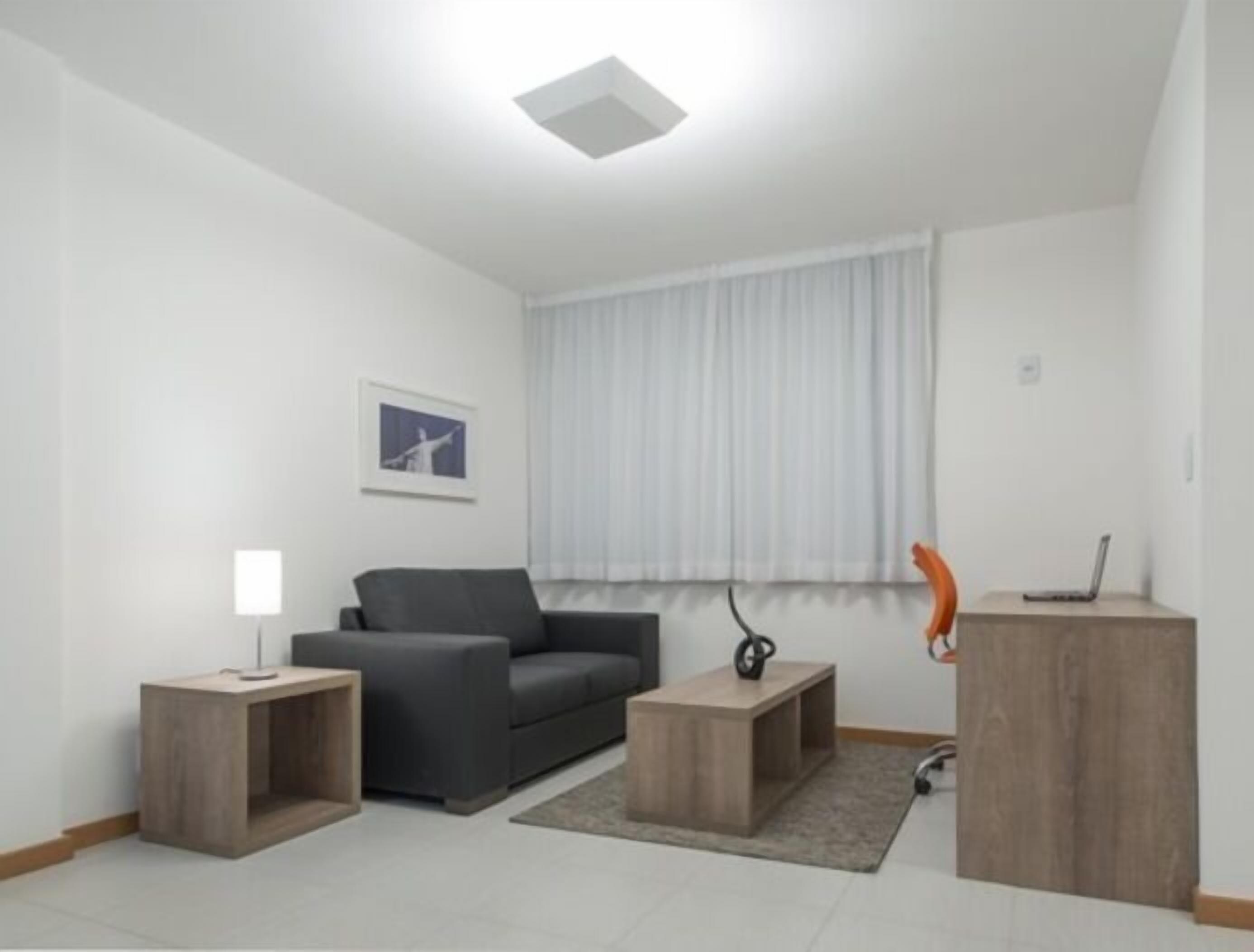 A modern living room with a grey sofa, a small wooden side table, a lamp, and a laptop on a wooden cabinet.