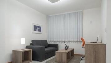 A modern living room with a grey sofa, a small wooden side table, a lamp, and a laptop on a wooden cabinet.