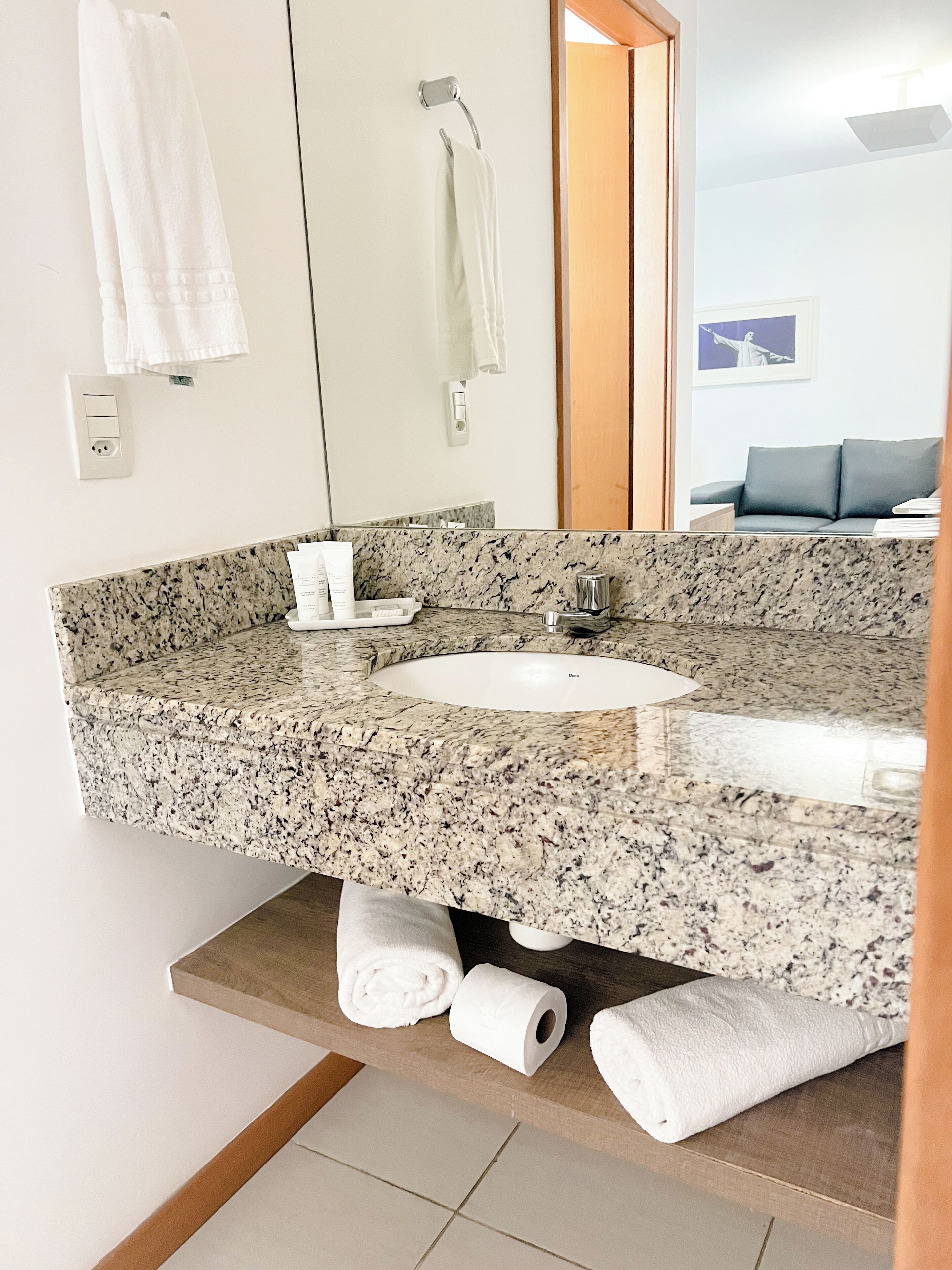 Un baño con encimera de granito, lavamanos, espejo y toallero.