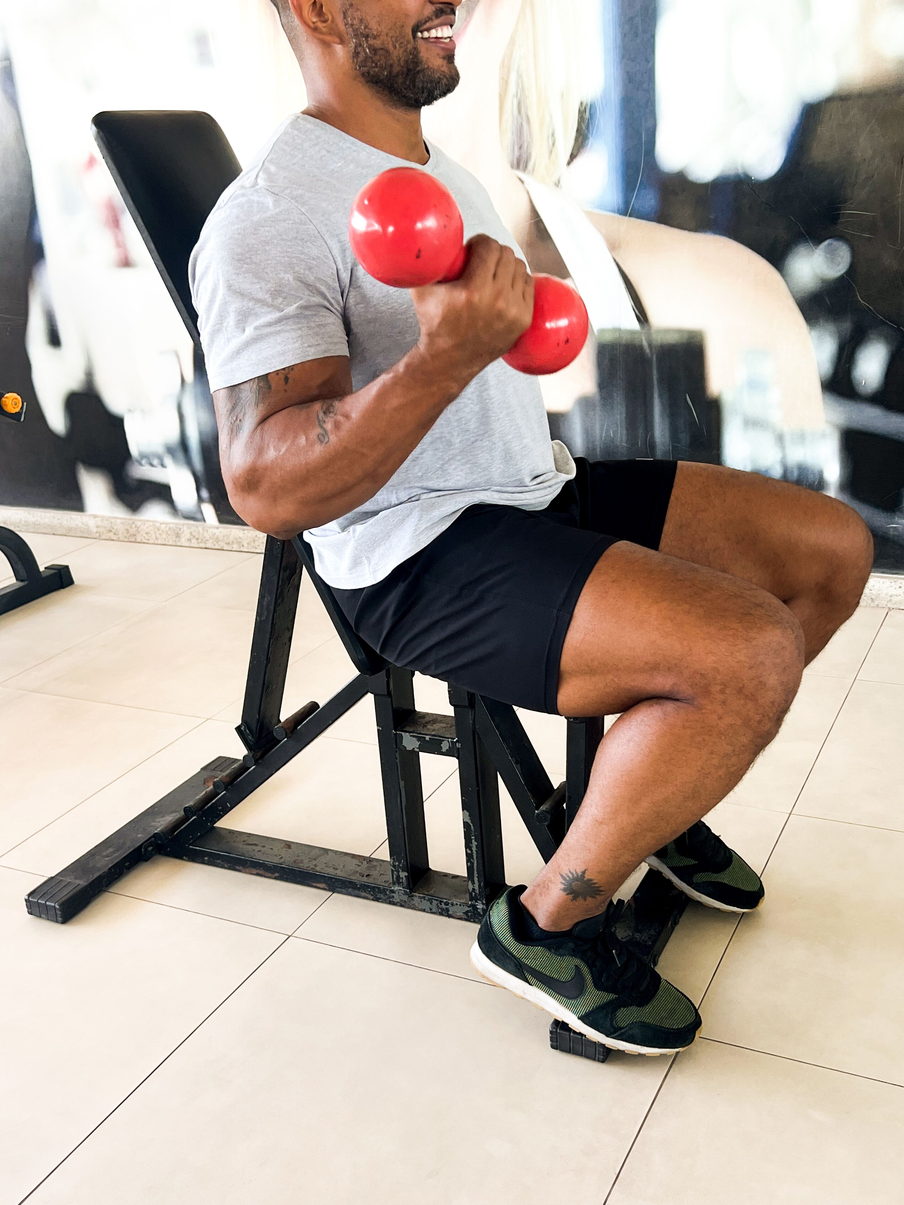 Une personne assise sur un banc de musculation, tenant des haltères rouges.