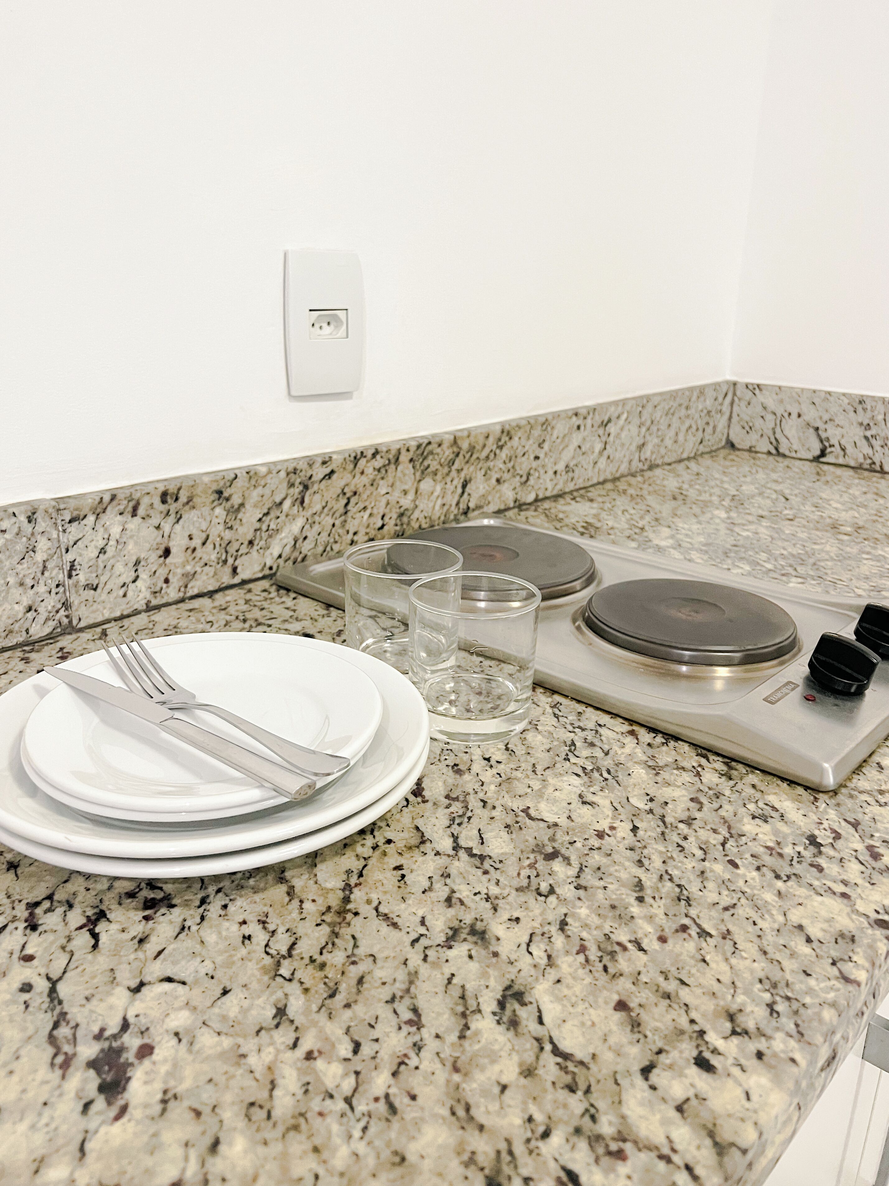 Una cocina con encimeras de granito, estufa y comedor con platos, cubiertos y vasos.
