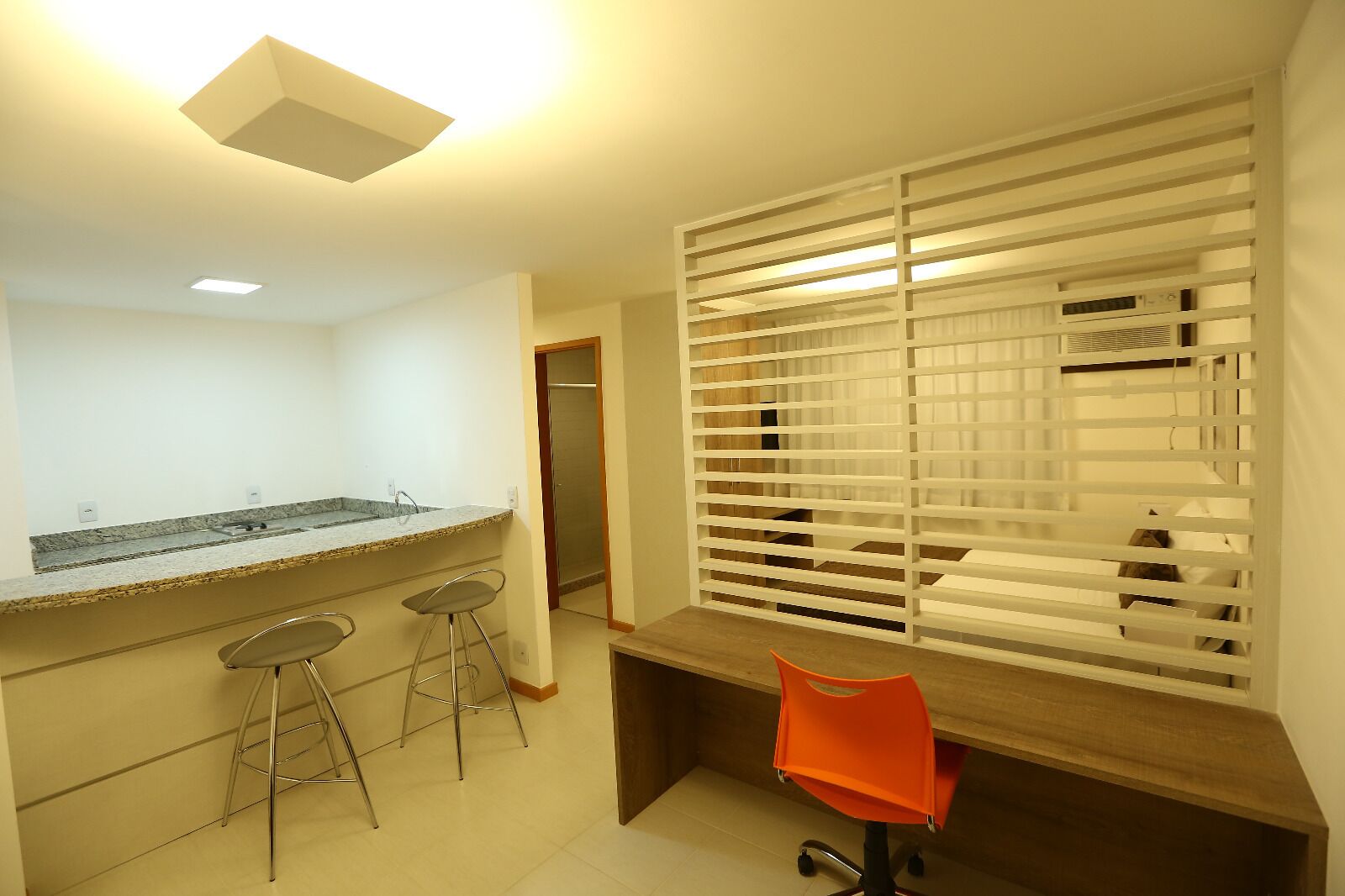 A kitchen with a granite countertop, three bar stools, a wooden table, and a window with blinds.