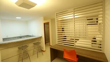 A kitchen with a granite countertop, three bar stools, a wooden table, and a window with blinds.