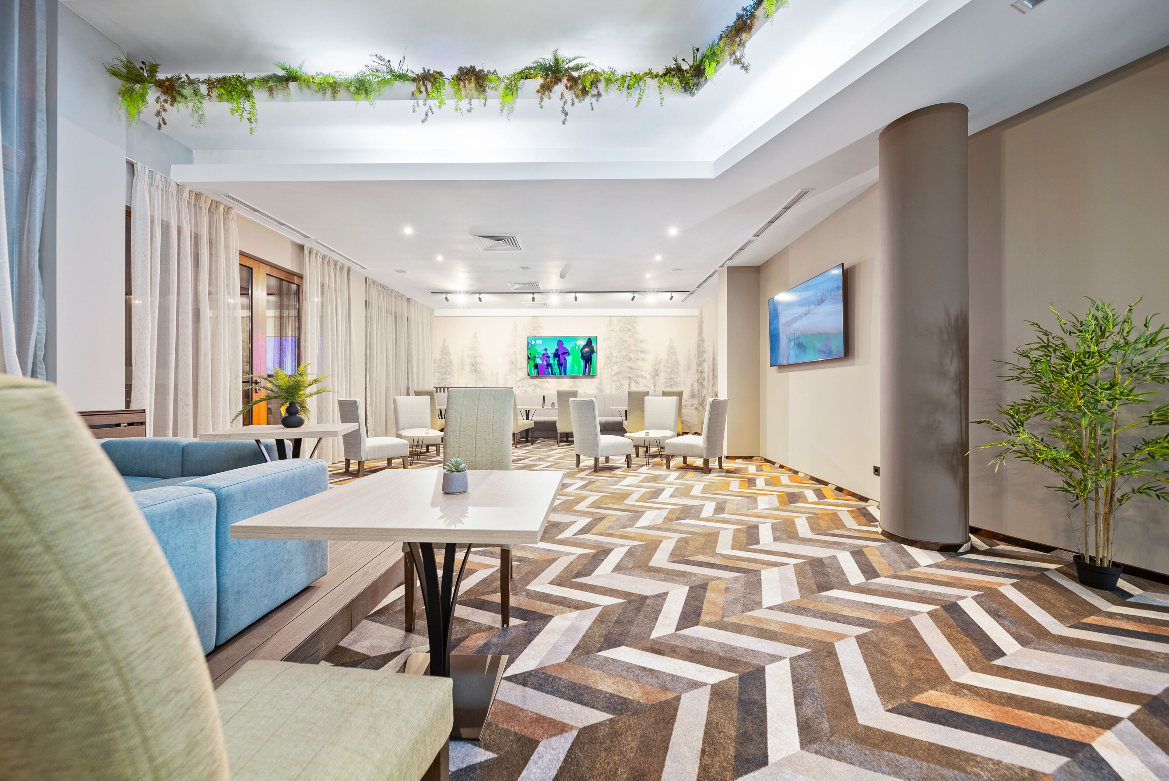 En moderne hotellobby med et geometrisk gulvmønster, en blå sofa og et fjernsyn i baggrunden.