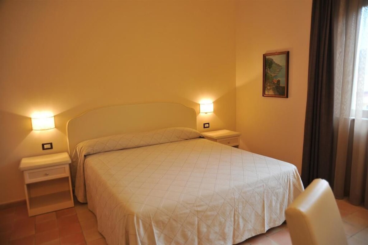 A hotel room with a bed, bedside tables, a chair, and a painting on the wall.