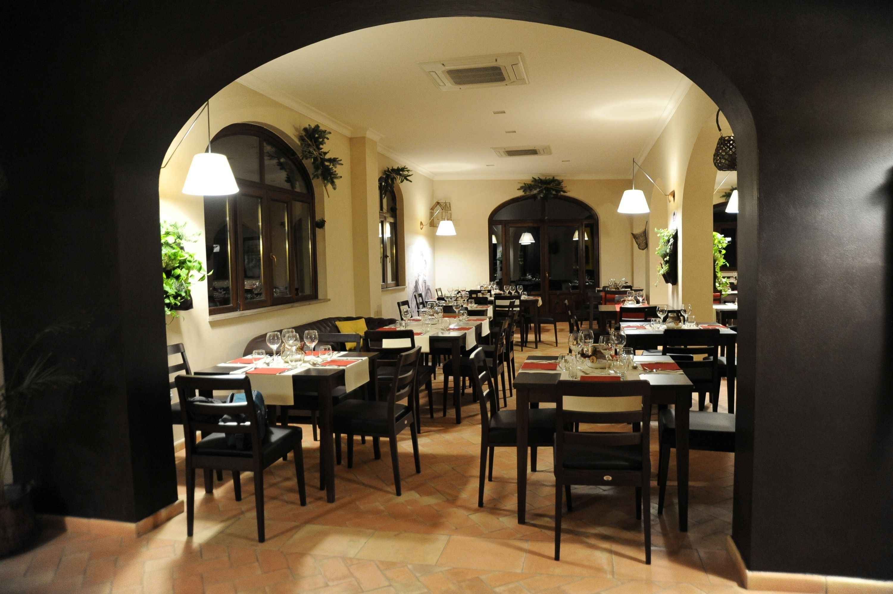 A restaurant with multiple tables and chairs, a tiled floor, and hanging lights.