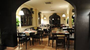 A restaurant with multiple tables and chairs, a tiled floor, and hanging lights.