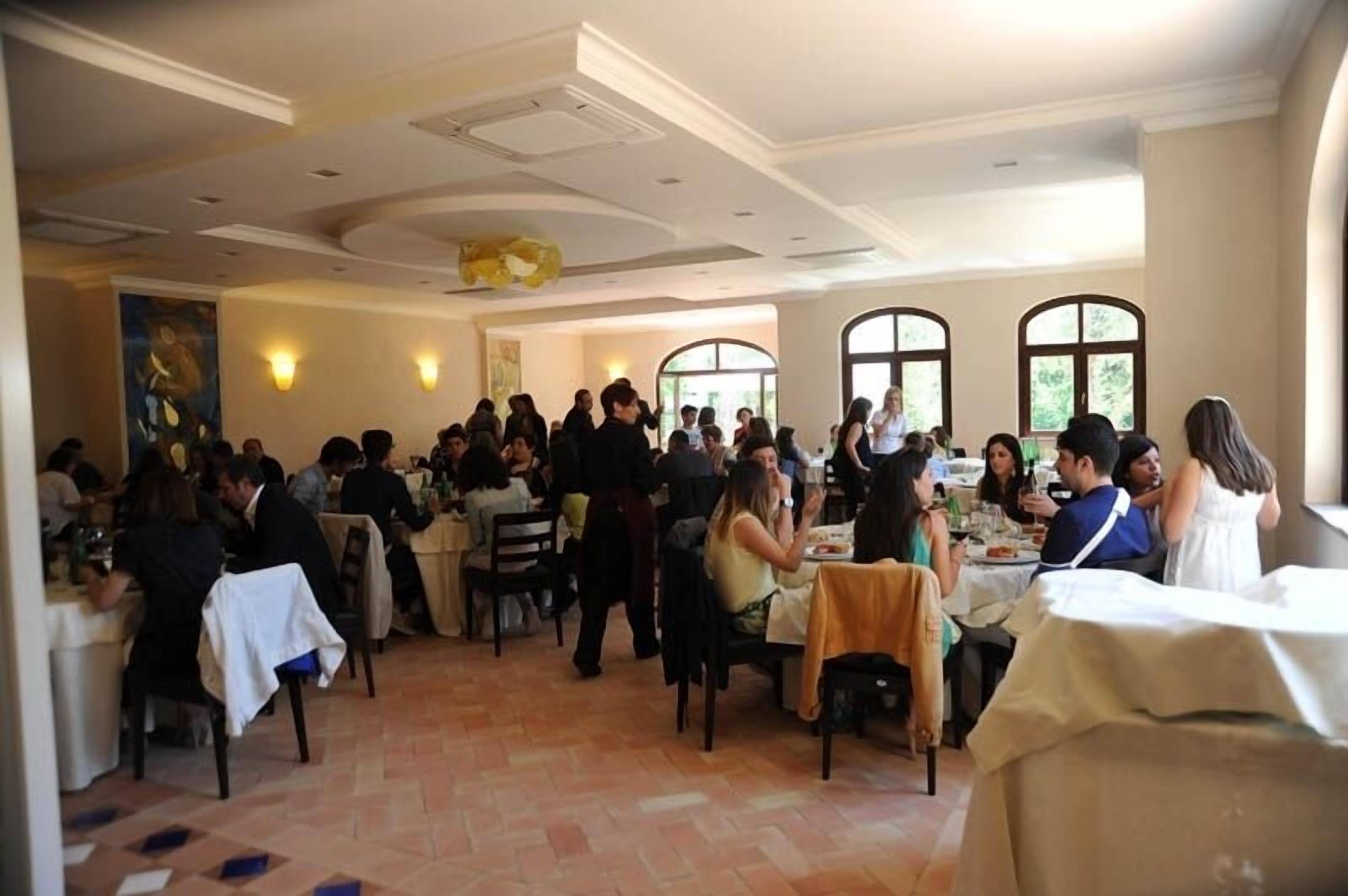 A spacious dining area with multiple tables and chairs, large windows, and a high ceiling with decorative moldings.