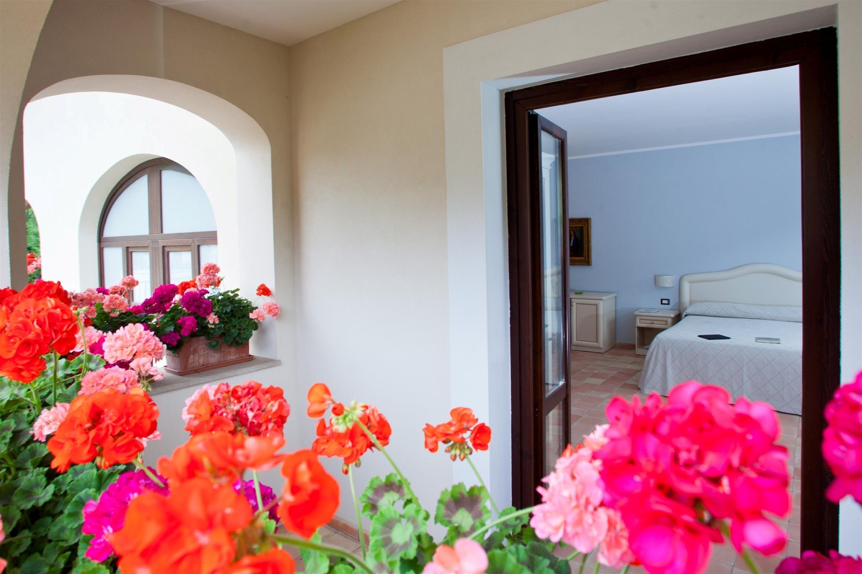 Ein Zimmer mit einem Bett, Nachttischen und einem Fenster mit Blumen.