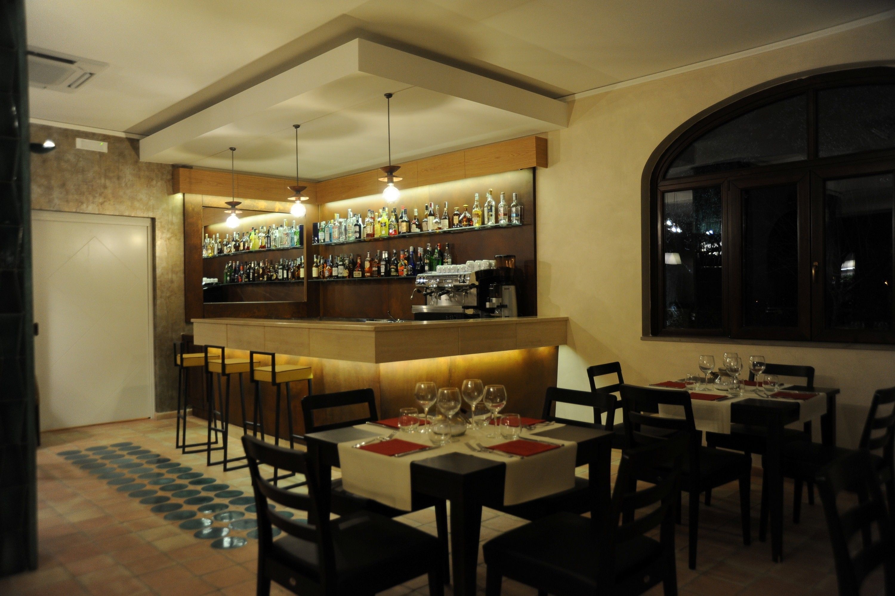 A restaurant with a bar area, multiple tables set for dining, and a view through a large window.