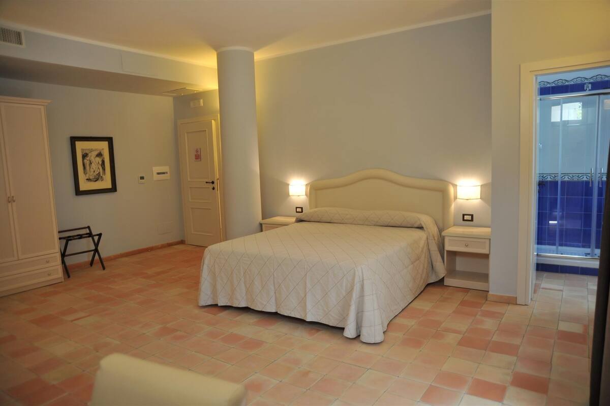 Une chambre à coucher comprenant un lit, des tables de chevet, une commode, un tableau encadré au mur et une porte donnant sur une autre pièce.