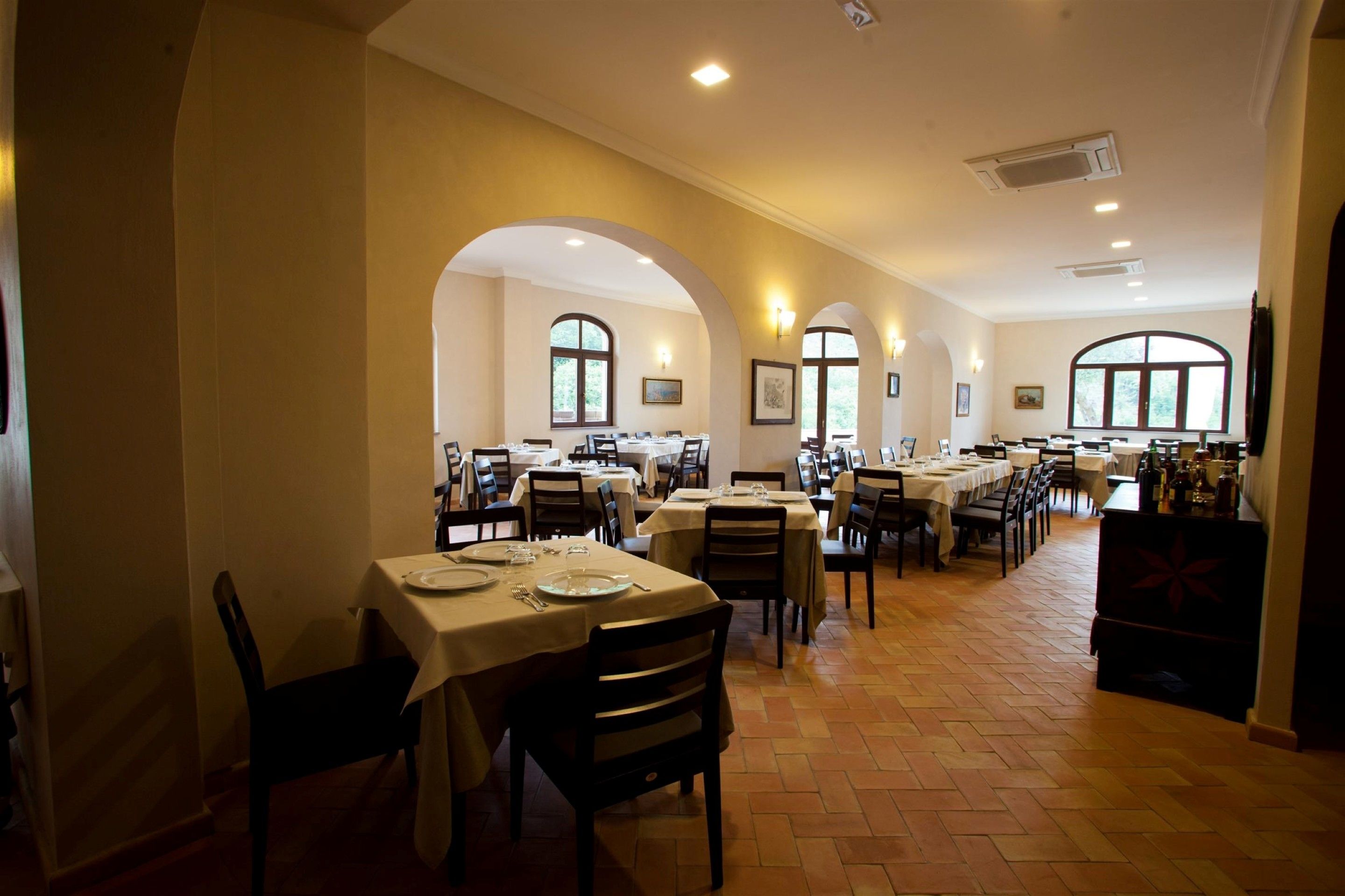 A spacious dining area with multiple tables and chairs, large windows, and a tiled floor.