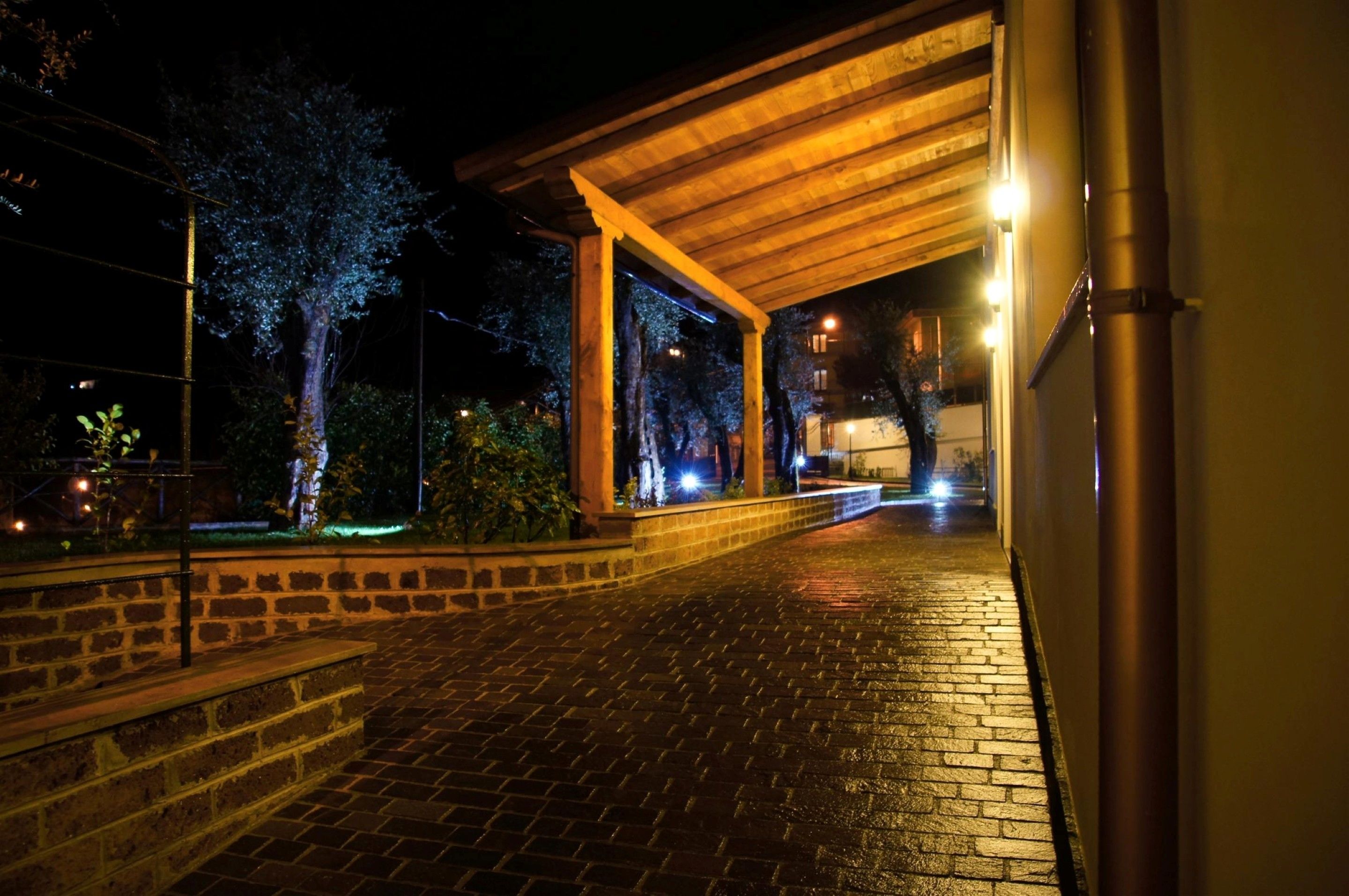 Vista nocturna de un espacio exterior cubierto con un sendero de ladrillo que conduce a la entrada de un edificio.
