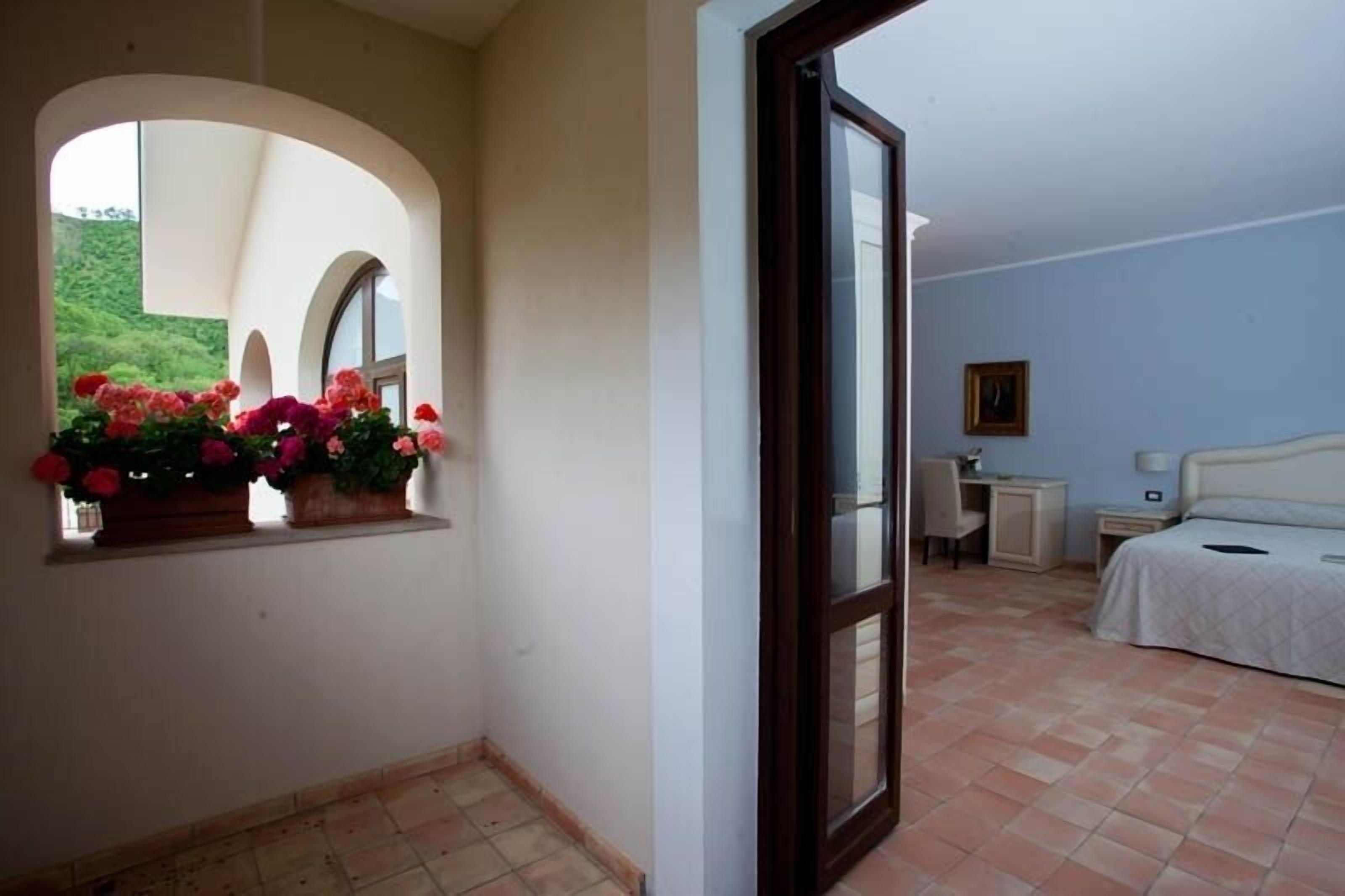 Une chambre à coucher avec un lit, un bureau, une chaise, une table de chevet et une fenêtre décorée de fleurs.