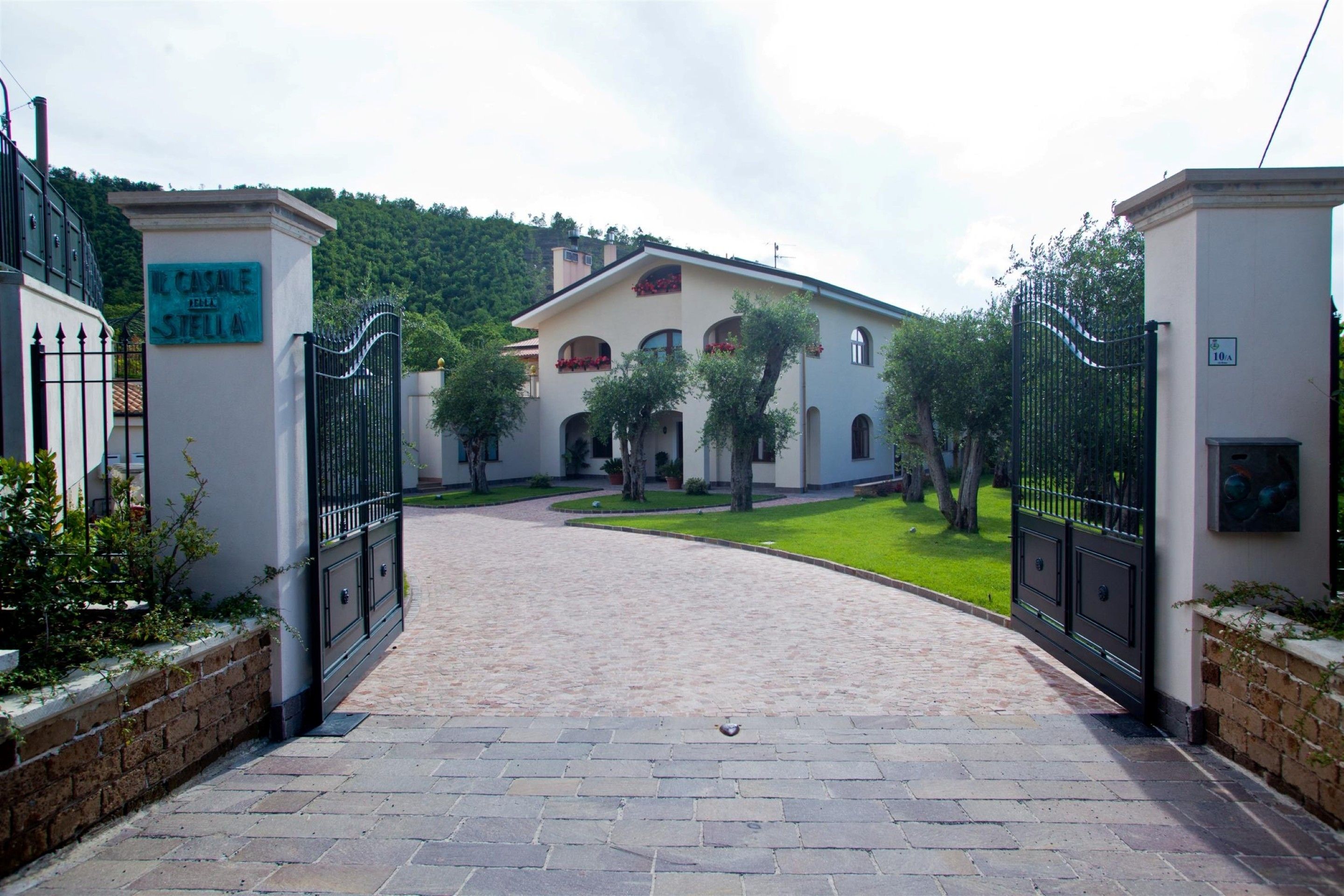 A gated entrance to a building with a paved driveway leading to a building with arched windows and a garden.