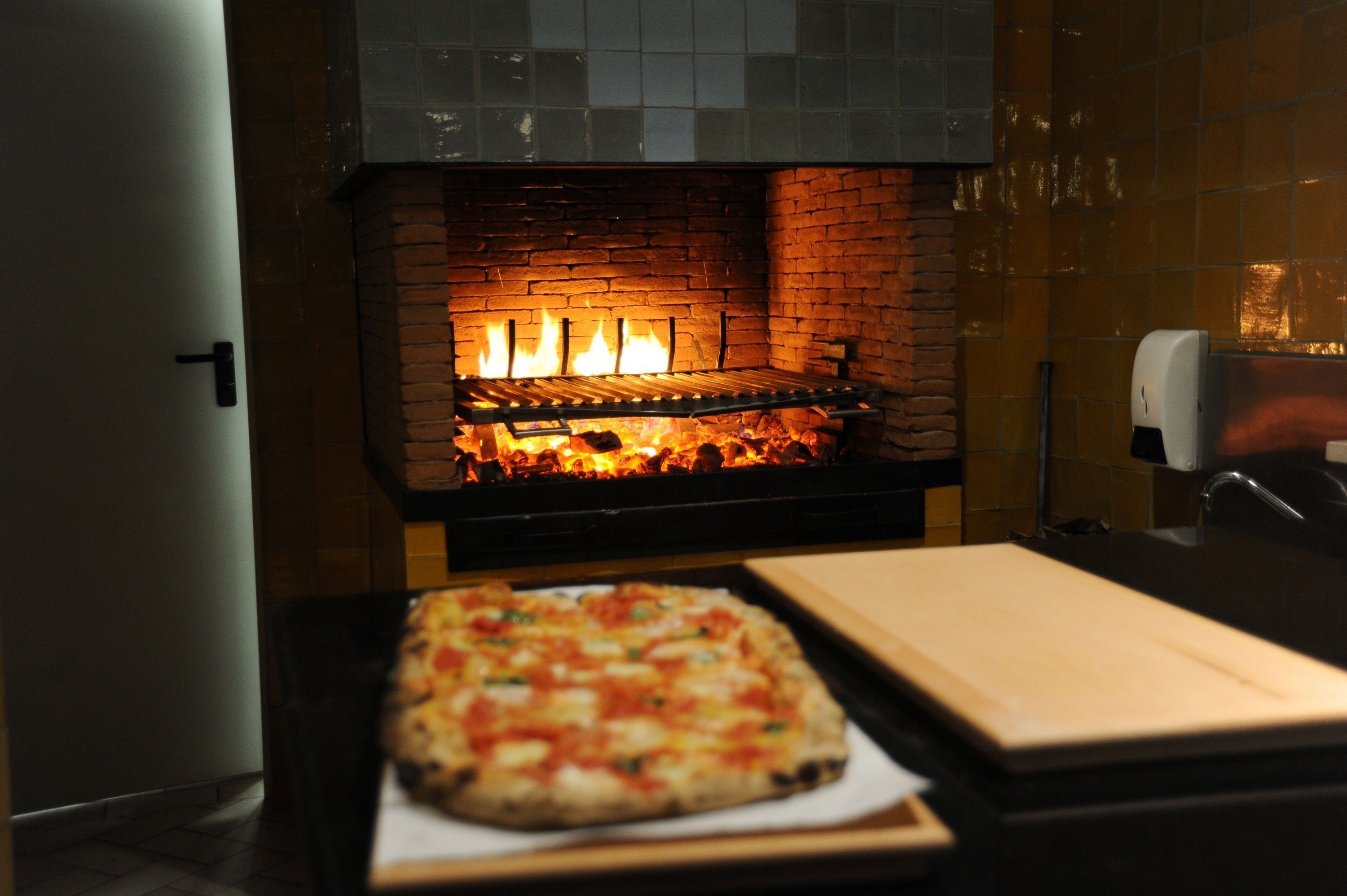 Ein Pizzaofen mit Backsteininnenraum und einer Pizza auf einem Tablett davor.