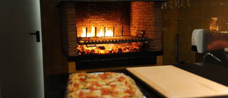 Ein Pizzaofen mit Backsteininnenraum und einer Pizza auf einem Tablett davor.