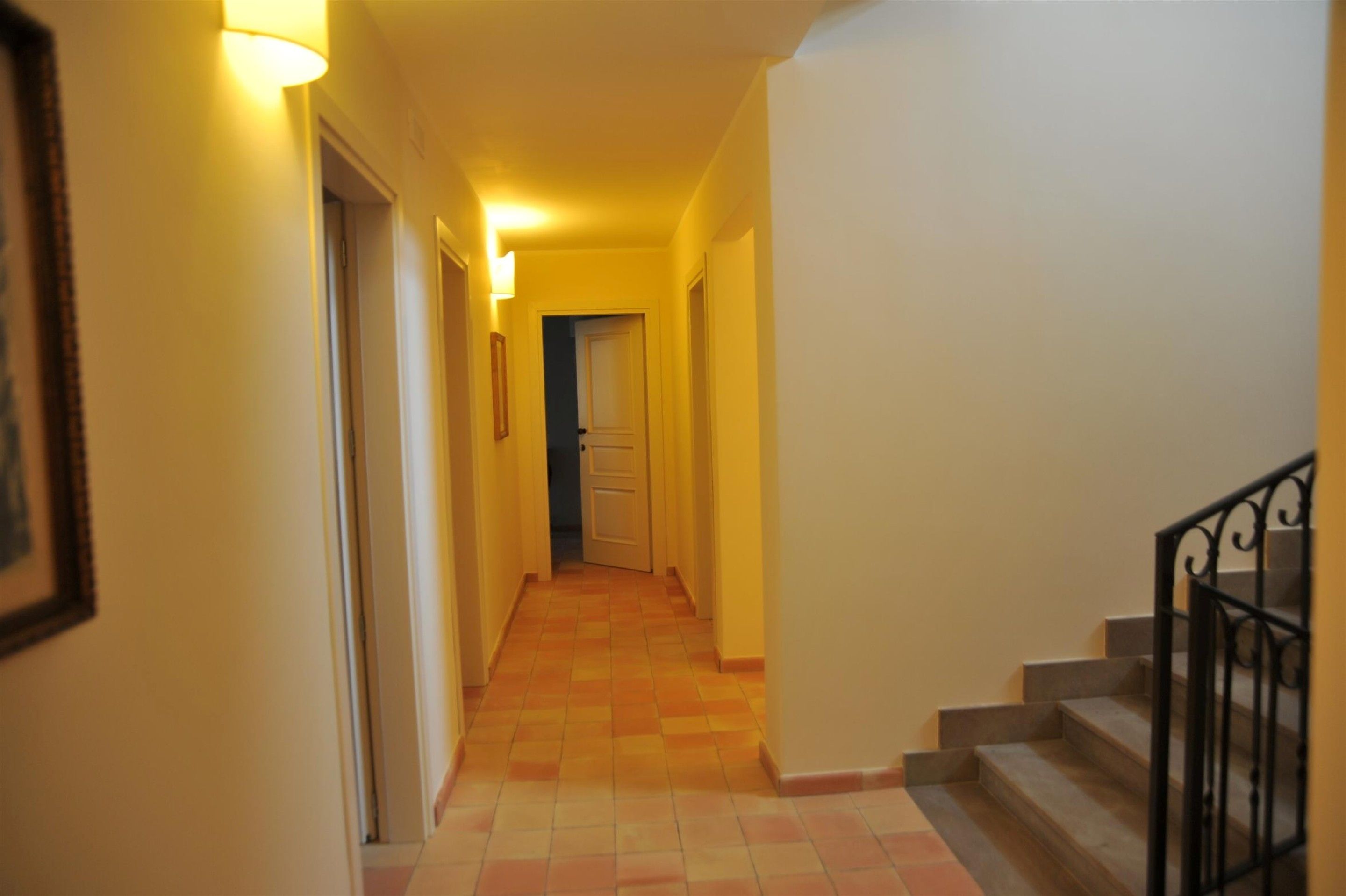 A hallway with a tiled floor, a staircase with black railings, and a door at the end.