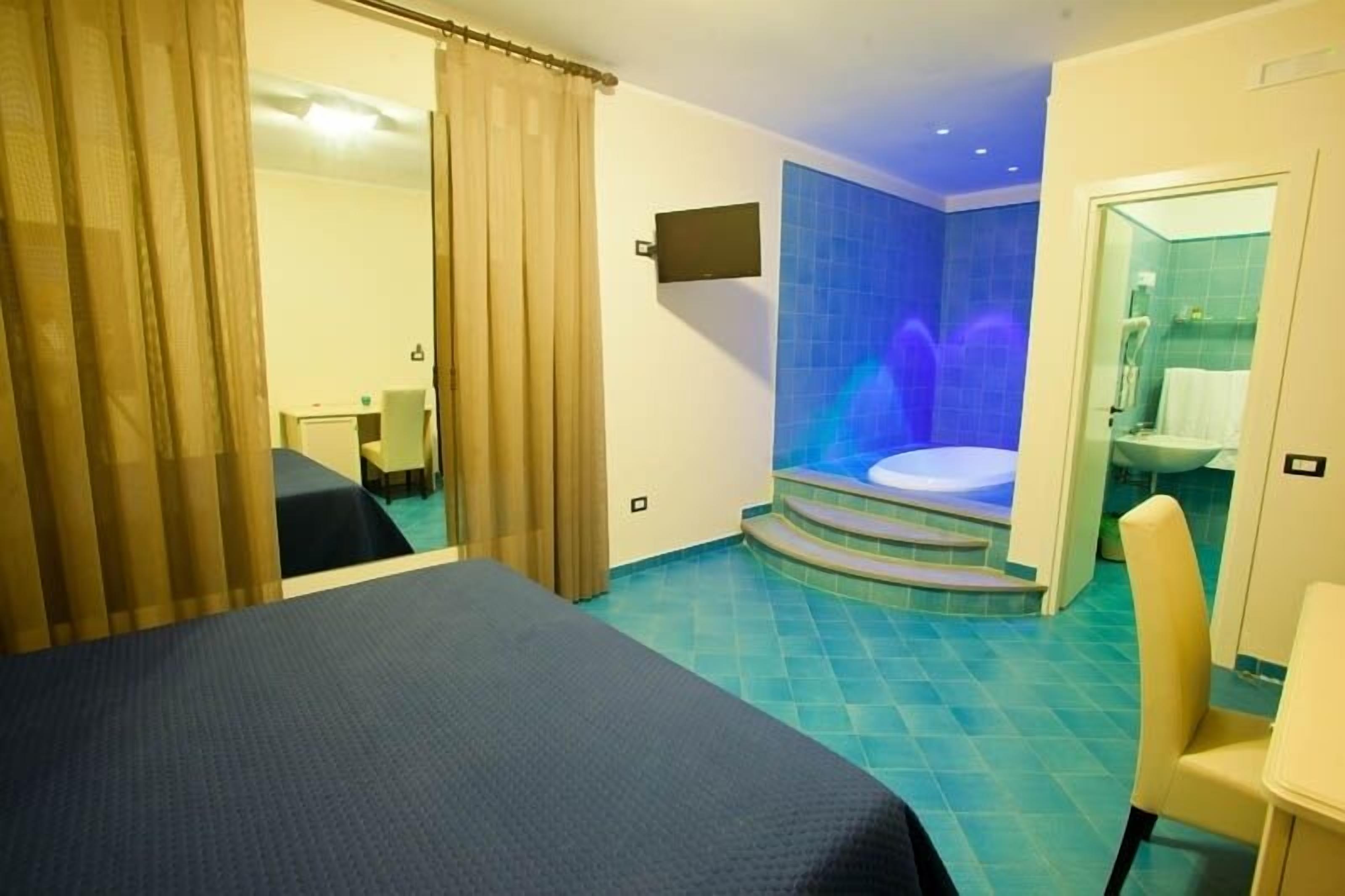 Habitació d'hotel amb un llit, un escriptori petit, una cadira i un bany amb banyera i plat de dutxa.