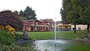 A courtyard with a fountain, a building with a red-tiled roof, and a well-maintained lawn. - Hotel Ristorante La Torretta (Bianze)