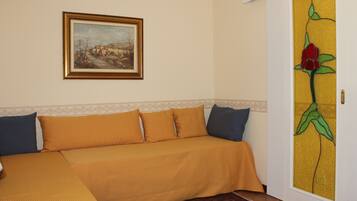 Una habitación con sofá cama, un cuadro enmarcado en la pared y una puerta con diseño floral.