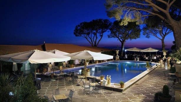 A poolside area with umbrellas, seating, and a view of the beach at dusk. - Grand Hotel Helio Cabala (Marino)